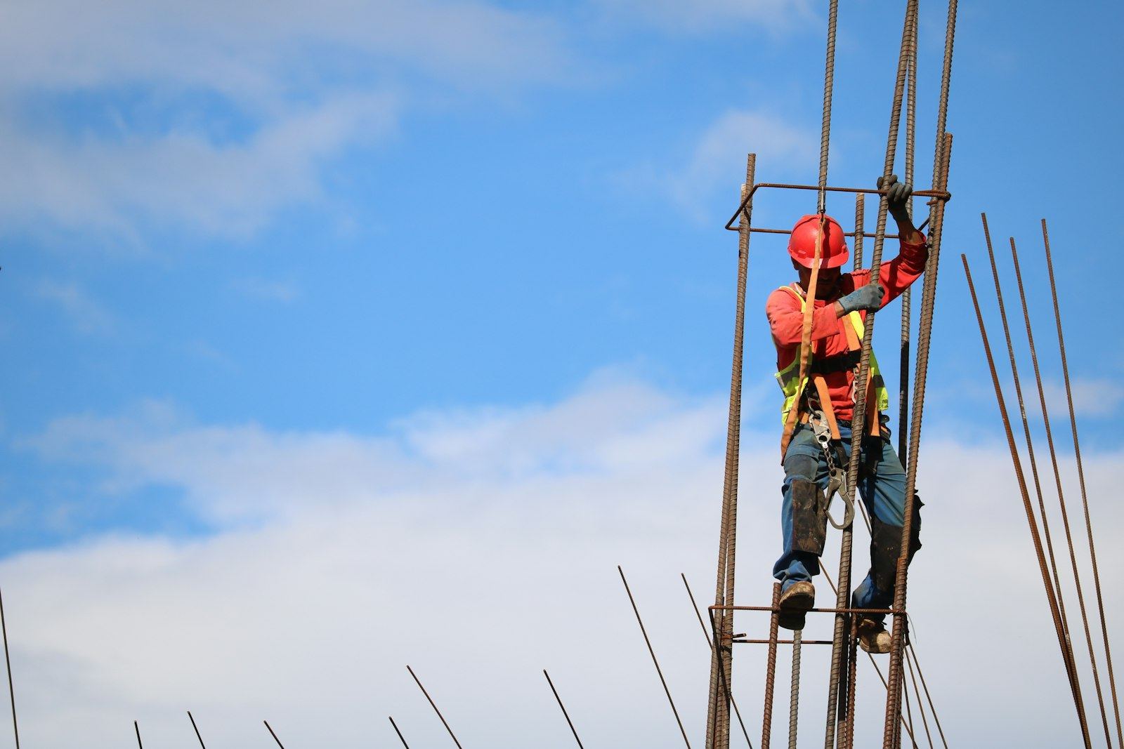 Ironworker tying rebar on a concrete column against a blue sky