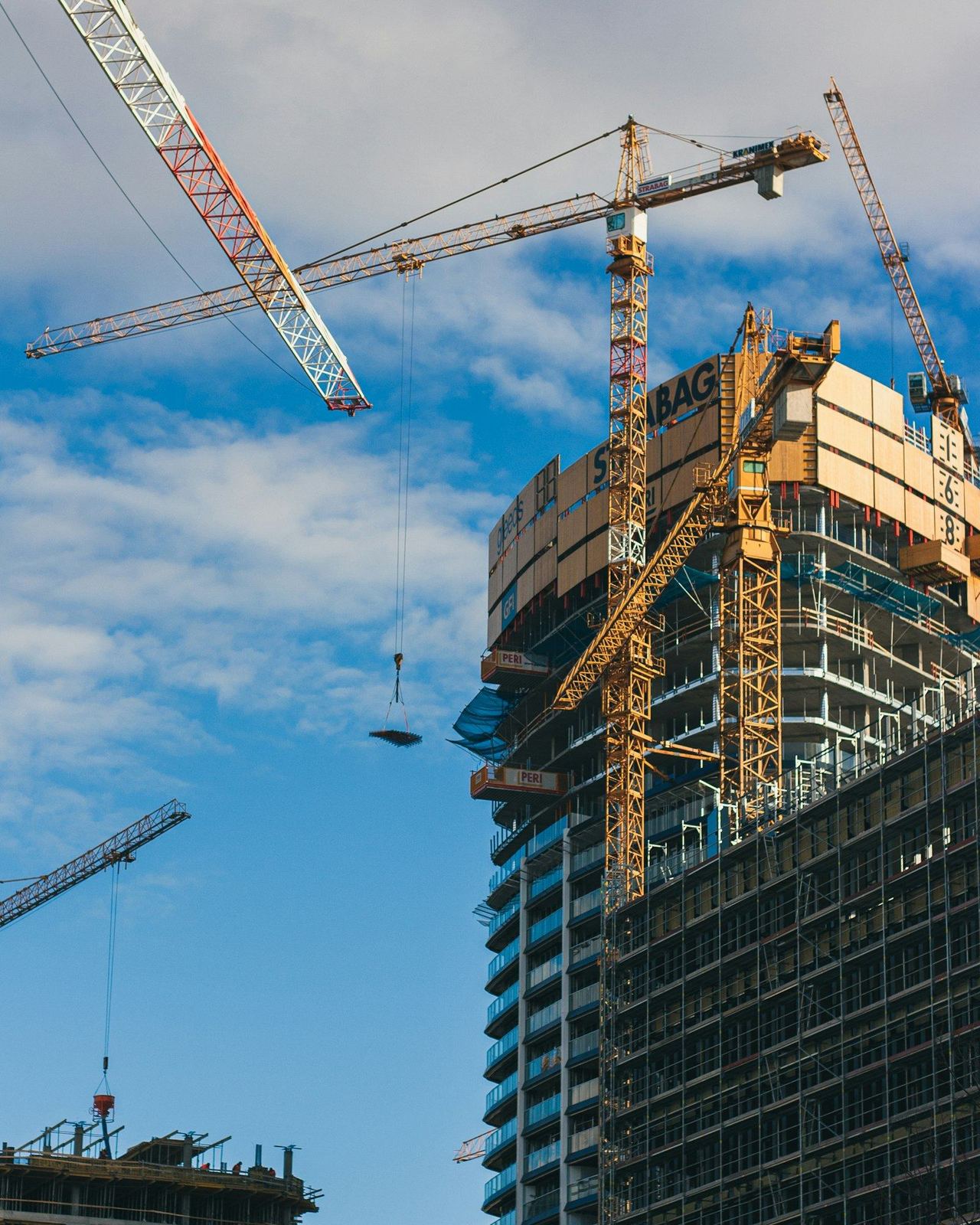 High-rise building under construction with tower cranes against a blue sky
